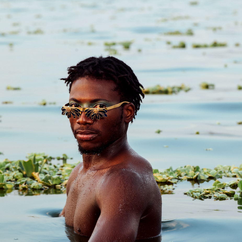 Person wearing sunglasses standing in water with greenery around